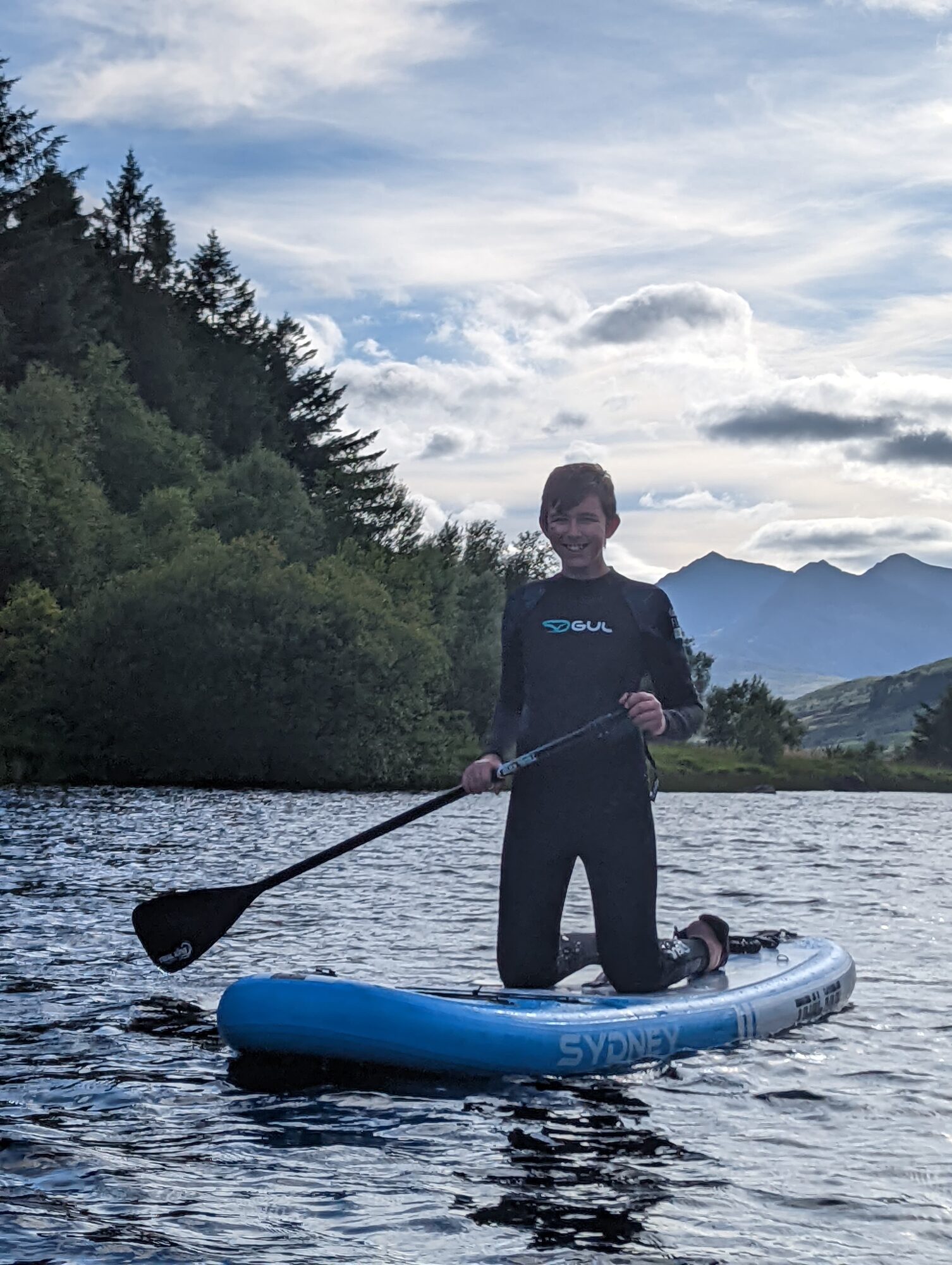 Boy paddleboarding on llynau mymbyr with Yr Wyddfa in the background